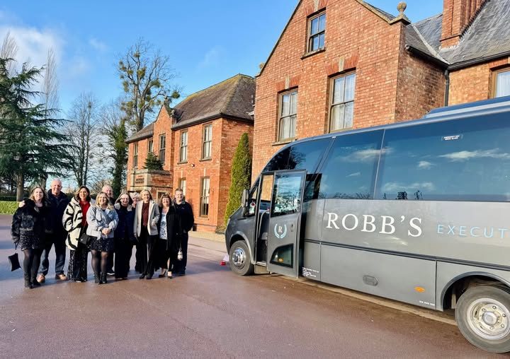 Corporate group posing with their Robb's minibus outside a country house