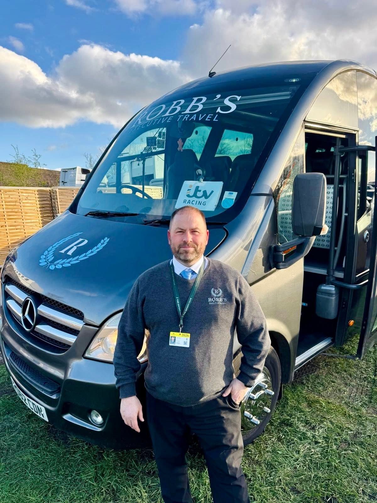 Robb's uniformed driver beside the minibus at a racecourse